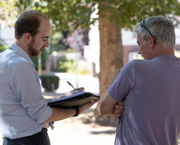 A member of staff is stood outside taking notes whilst talking to a resident