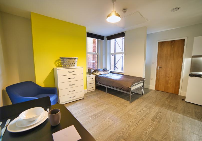 Studio flat with a bed, kitchenette, furniture and bright yellow painted wall