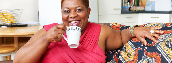 A resident sat in her lounge, drinking a coffee. She is smiling. 