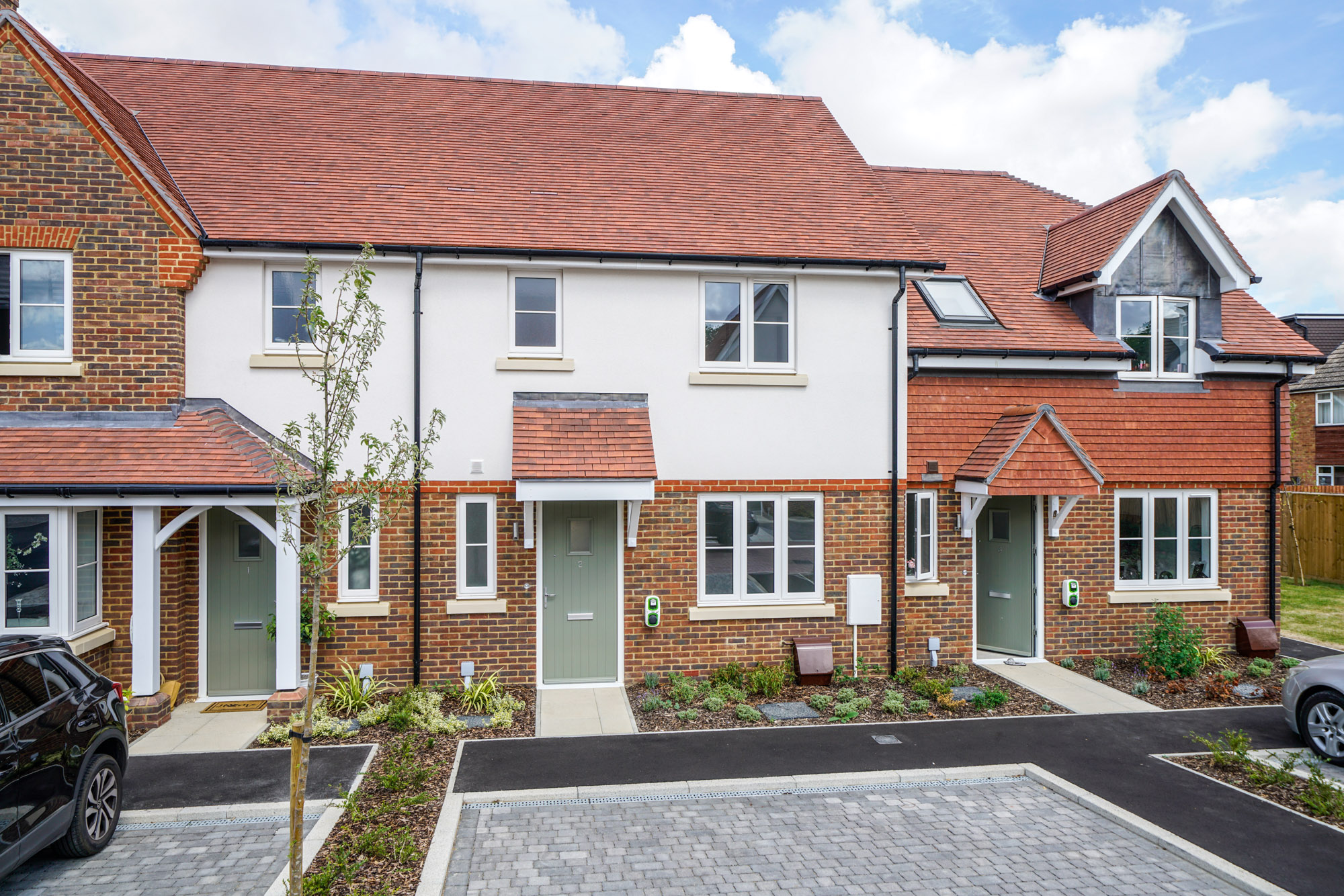 New build houses, which are white and brick. They have a parking space outside.