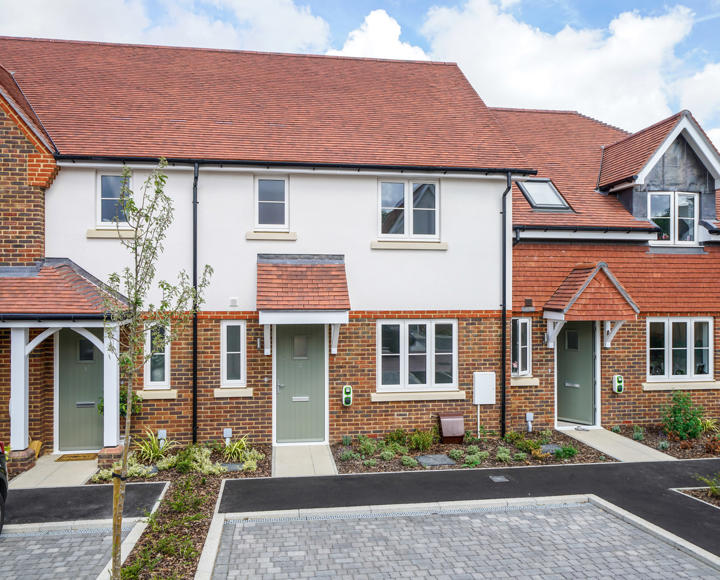 New build houses, which are white and brick. They have a parking space outside.