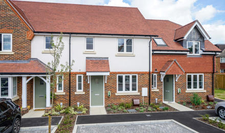 New build houses, which are white and brick. They have a parking space outside.