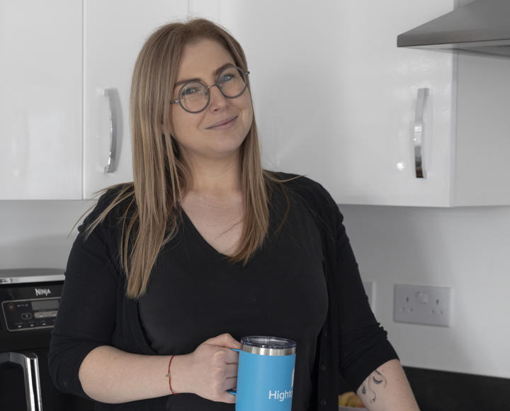 A female Hightown resident standing in her kitchen with a Hightown branded mug