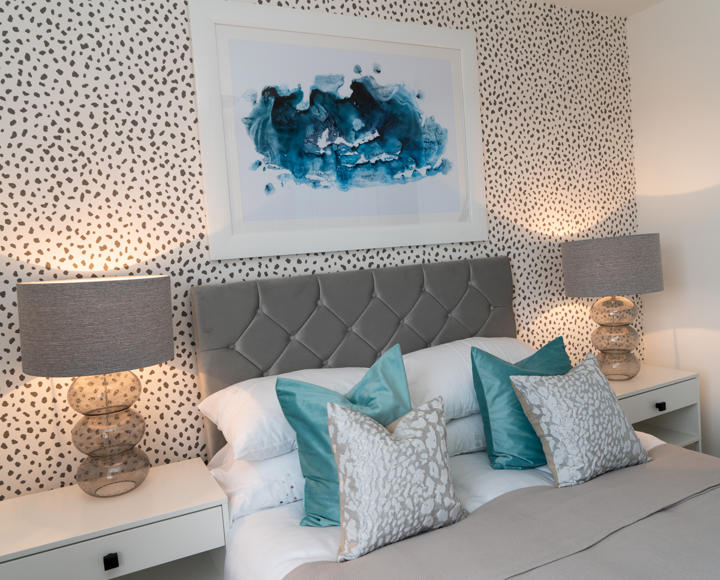 A stock image of the top half of a double bed with its headboard, cushions and bedside tables