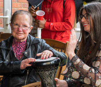 Two women playing bongo drums and smiling