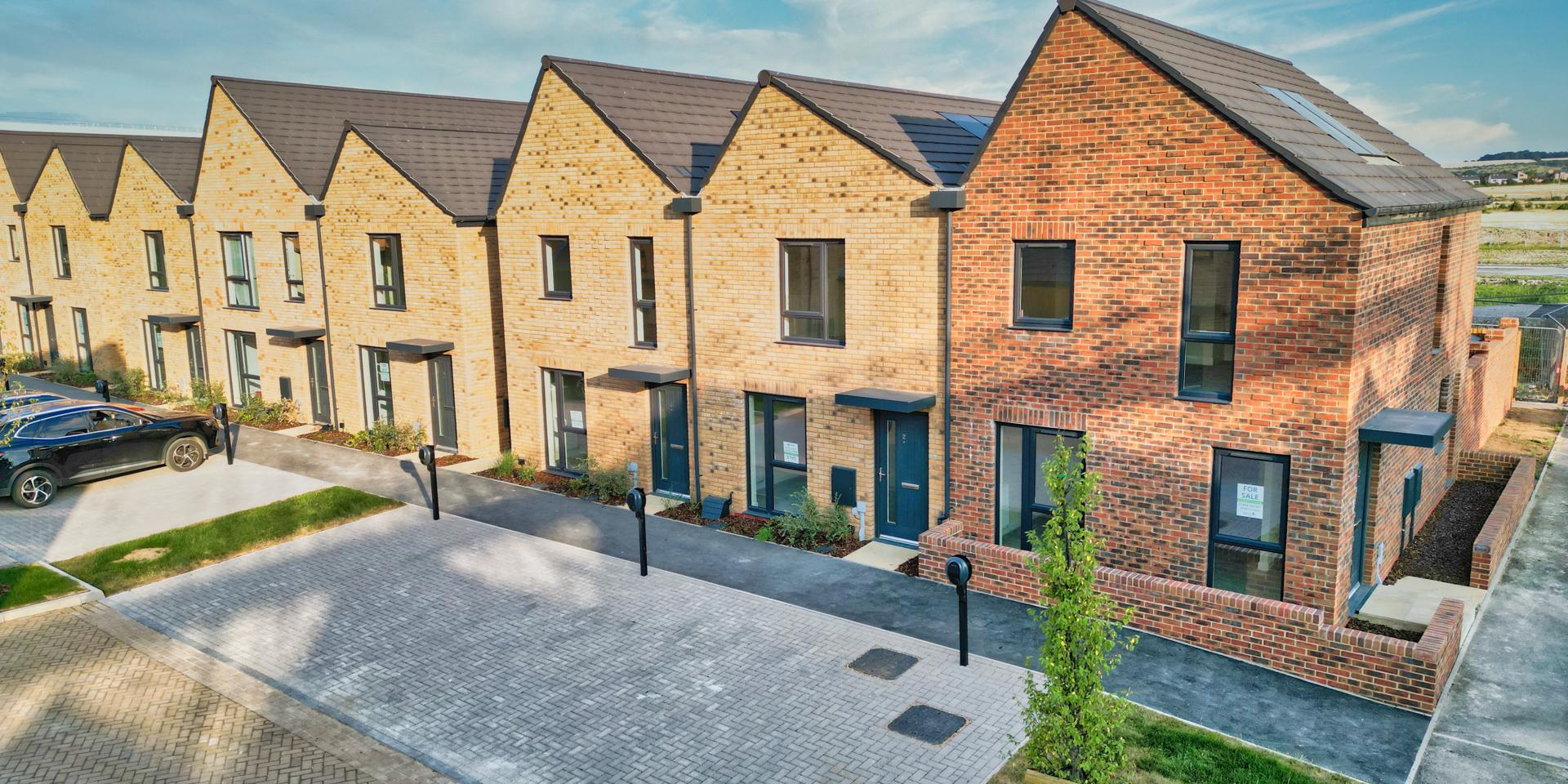 The houses are terraced or semi detached with EV parking to the front and areas of grass