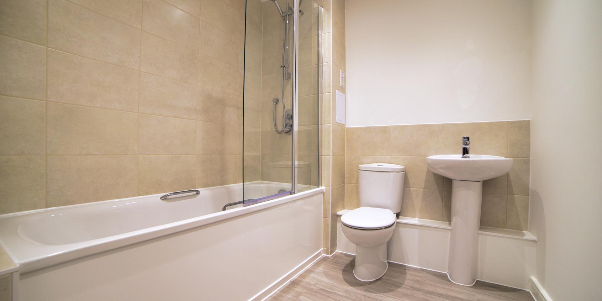 There is a white bathroom suite with a thermostatic shower over the bath and glass shower screen. There are wall tiles around the bath and as a splashback to the basin and toilet