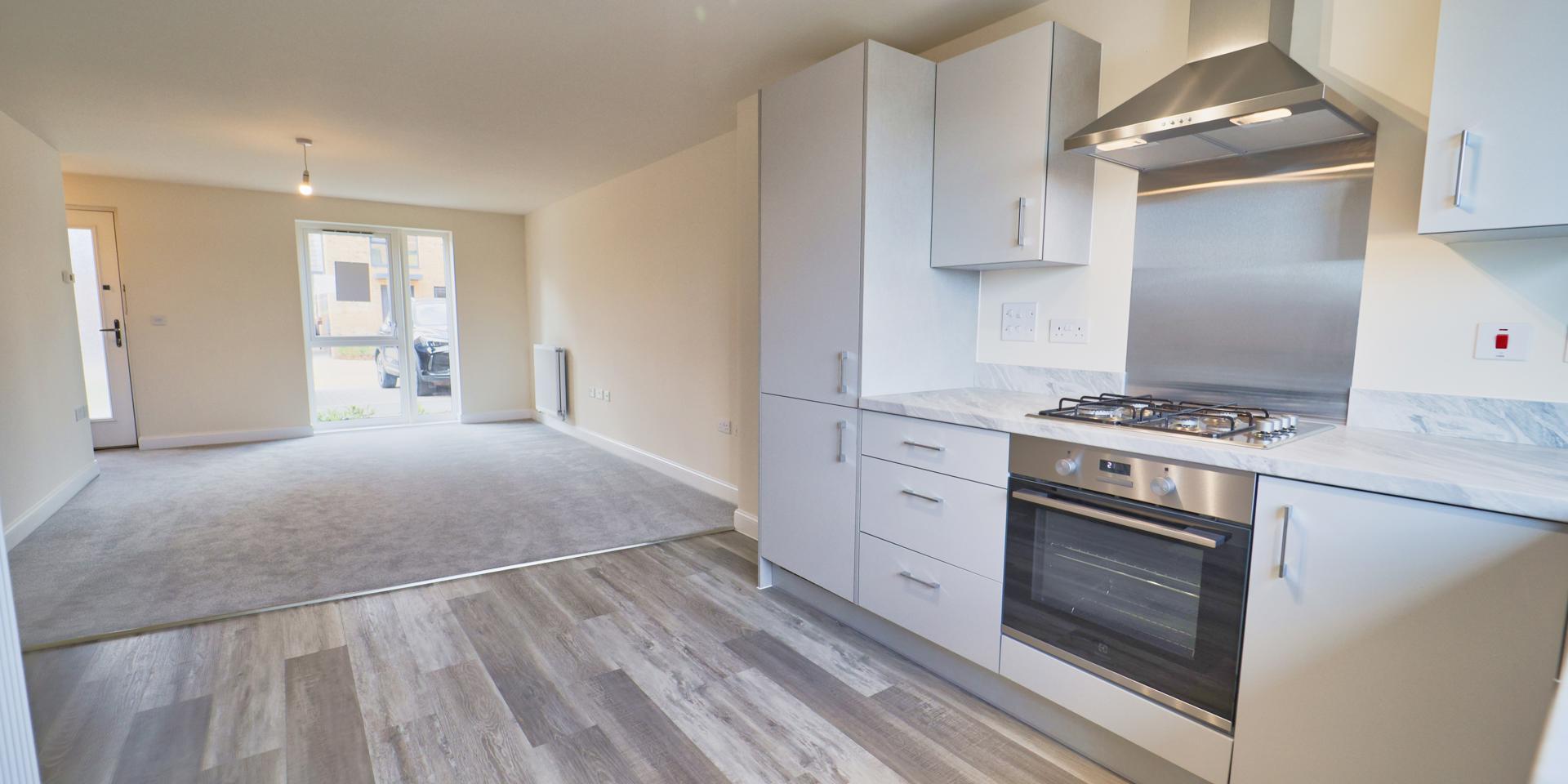 A view across the living/dining room from the kitchen. The kitchen floor is vinyl and the living/dining room is carpeted.