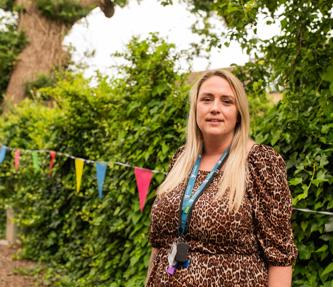 Woman smiling and standing in front of garden hedge with colourful bunting attached