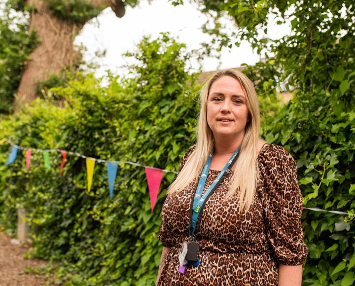 Woman smiling and standing in front of garden hedge with colourful bunting attached