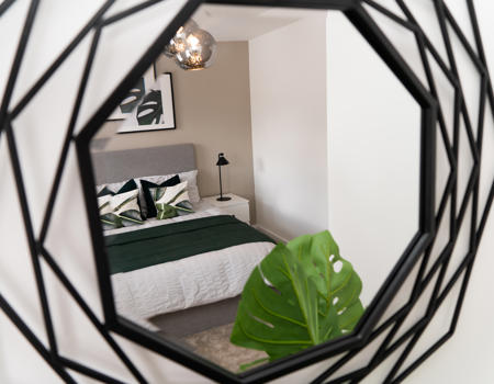 A black metal mirror showing the reflection of a double bed