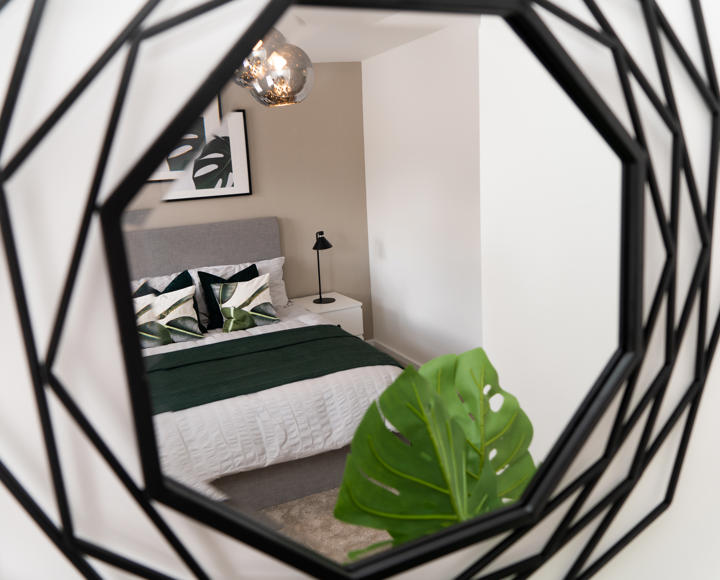 A black metal mirror showing the reflection of a double bed