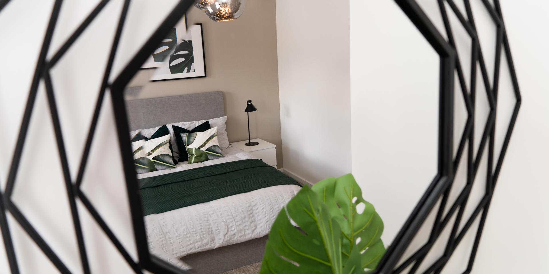 A black metal mirror showing the reflection of a double bed