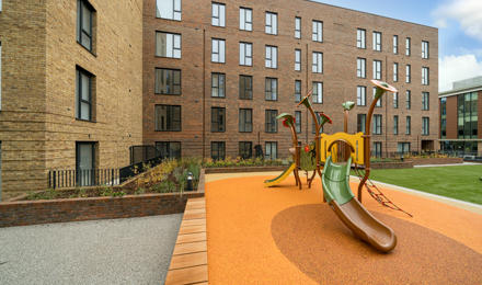 A playground with a slide in front of a new block of flats.