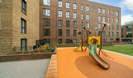 A playground with a slide in front of a new block of flats.