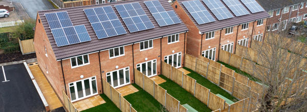 A row of the backs of houses with solar panels on the roof. Each house has its own back garden. 