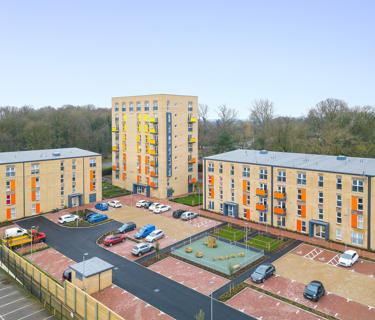 Aerial view off 4 blocks of flats. There are parking spaces and a play park in the middle.