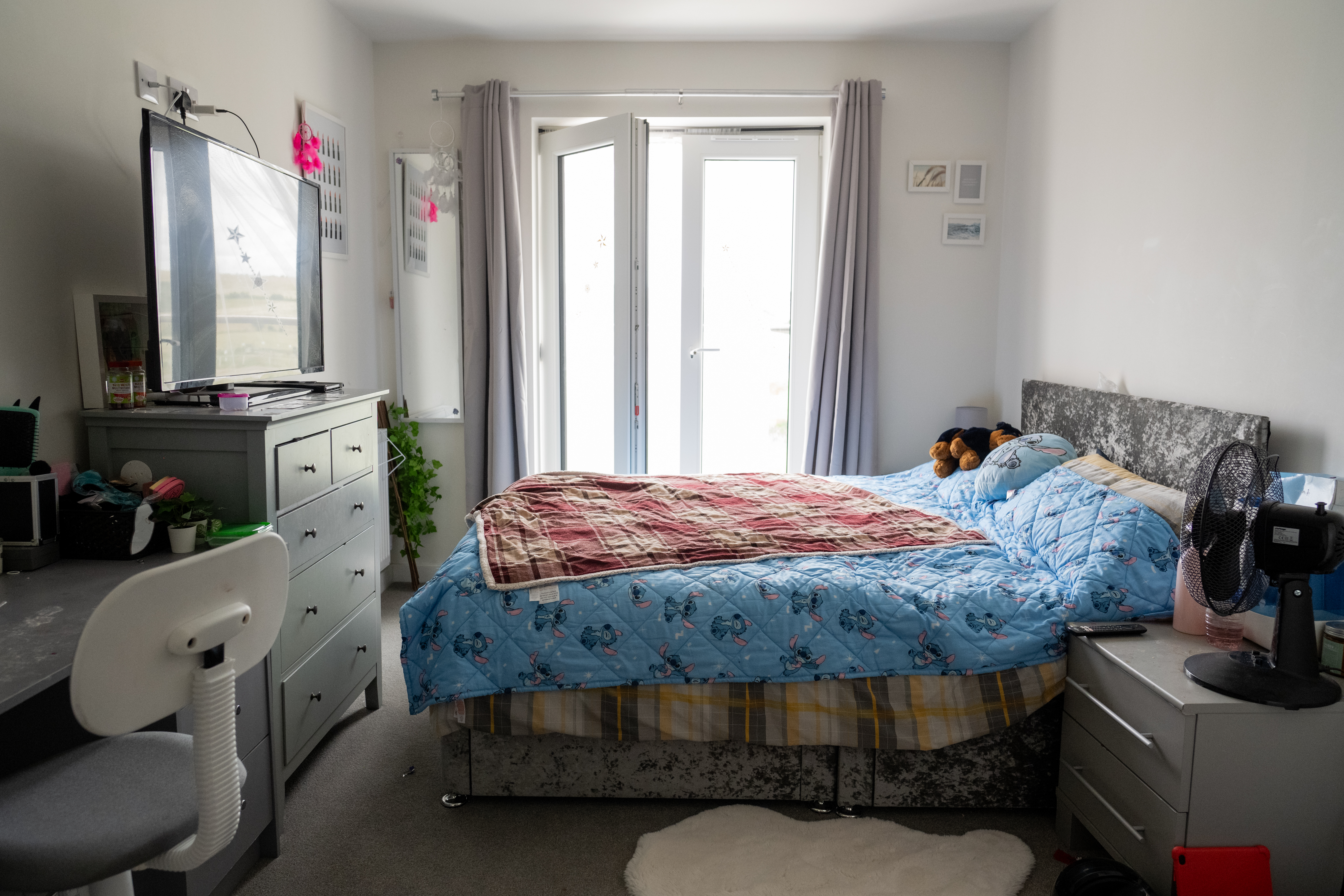 A bedroom containing a bed, desk, chest of drawers and a side table. 