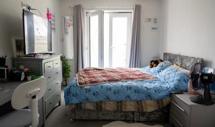 A bedroom containing a bed, desk, chest of drawers and a side table. 