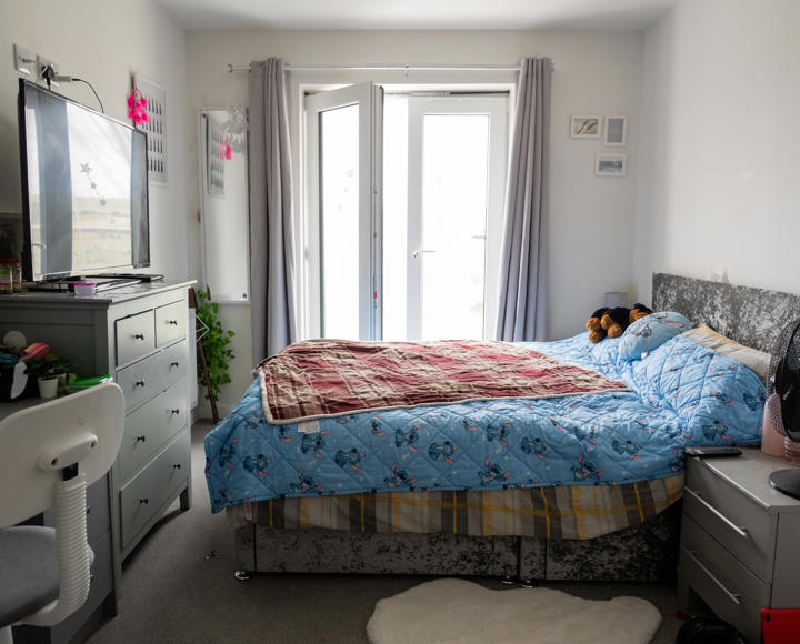 A bedroom containing a bed, desk, chest of drawers and a side table. 