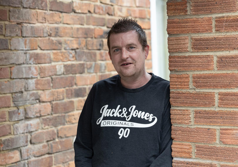 Man smiling, standing against a wall