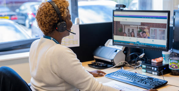A female member of staff helping a resident on a phone call and using her computer.