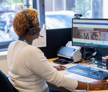 A female member of staff helping a resident on a phone call and using her computer.