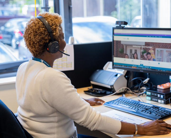 A female member of staff helping a resident on a phone call and using her computer.