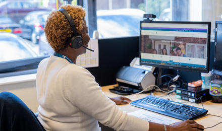 A female member of staff helping a resident on a phone call and using her computer.