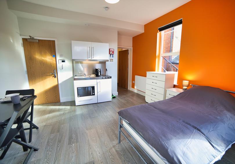 Studio flat with a bed, kitchenette, furniture and bright orange wall