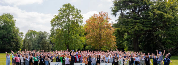 Hightown staff waving outside with Hightown logo and sign saying 'Building homes. Supporting people.'