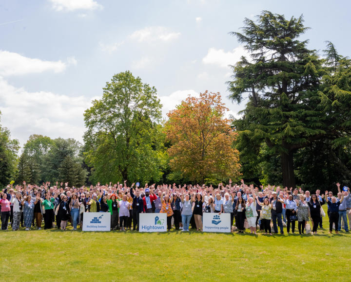 Hightown staff waving outside with Hightown logo and sign saying 'Building homes. Supporting people.'