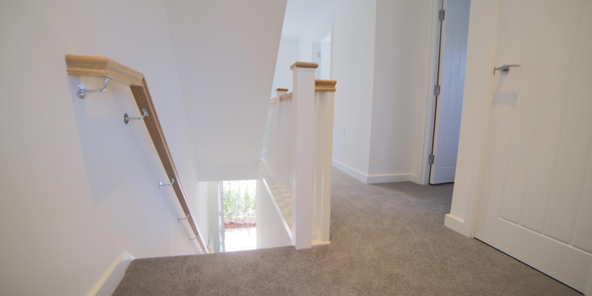 The landing banister is painted white with a modern wooden hand rail.