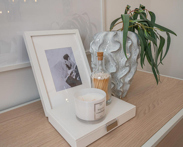 A stock image of a photo frame, candle and vase on a chest of drawers