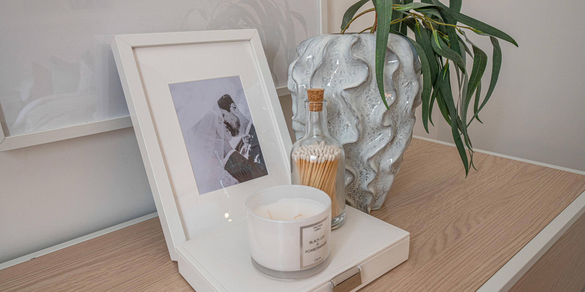 A stock image of a photo frame, candle and vase on a chest of drawers