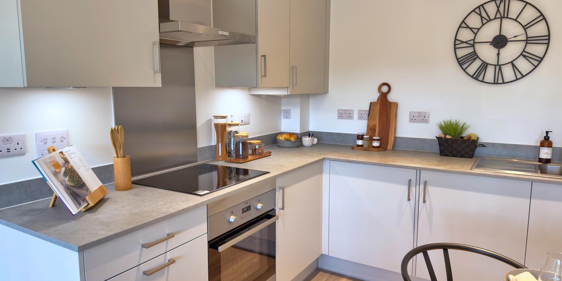 The kitchen is l-shaped and has light grey, matt cupboards with a grey work top