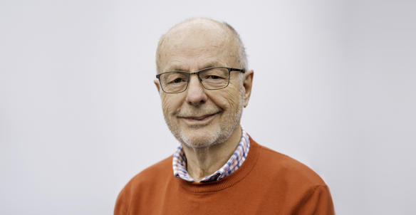 Headshot of board member, Alan Head. He is wearing glasses, a bright red jumper and a red, white and blue checked shirt. He has brown eyes and white/grey hair.
