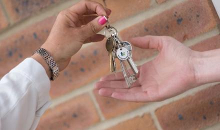 someone handing someone else a set of keys in front of a brick wall