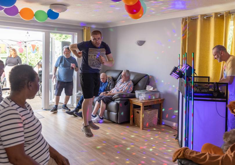A service user dancing to music as a dj plays, while other service users look on