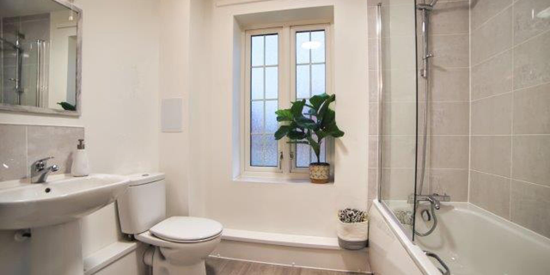 View of the spacious bathroom with the bath, shower, toilet and wash hand basin. There is also a window in the bathroom.