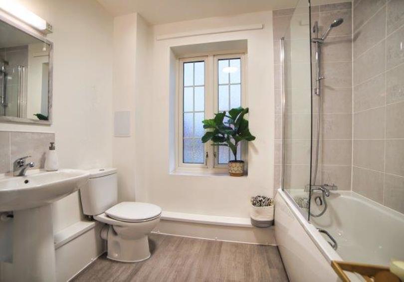 View of the spacious bathroom with the bath, shower, toilet and wash hand basin. There is also a window in the bathroom.
