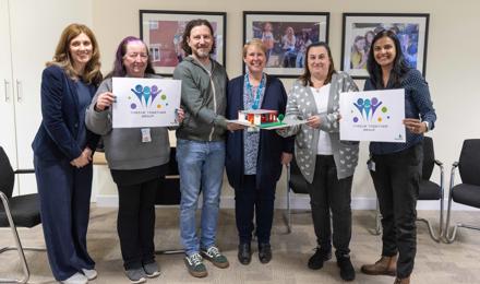 Five women and one man standing up and smiling, holding signs that read Thrive Together Group
