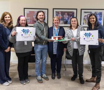 Five women and one man standing up and smiling, holding signs that read Thrive Together Group
