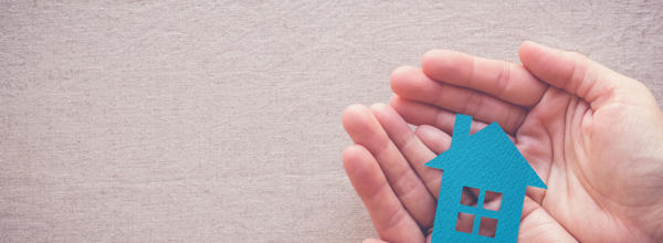 Someone holding cardboard cut out of a blue house in the palm of their hands.