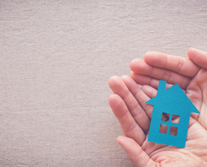 Someone holding cardboard cut out of a blue house in the palm of their hands.