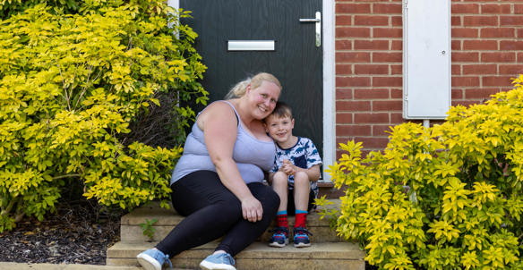 A mother and son sat outside of a house on the front doorstep.