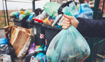 Someone holding a bin bag next to an overflowing bin store