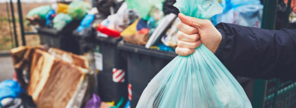 Someone holding a bin bag next to an overflowing bin store