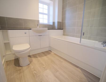 The bathroom has a white suite with built-in vanity unit and glass shower screen to the bath