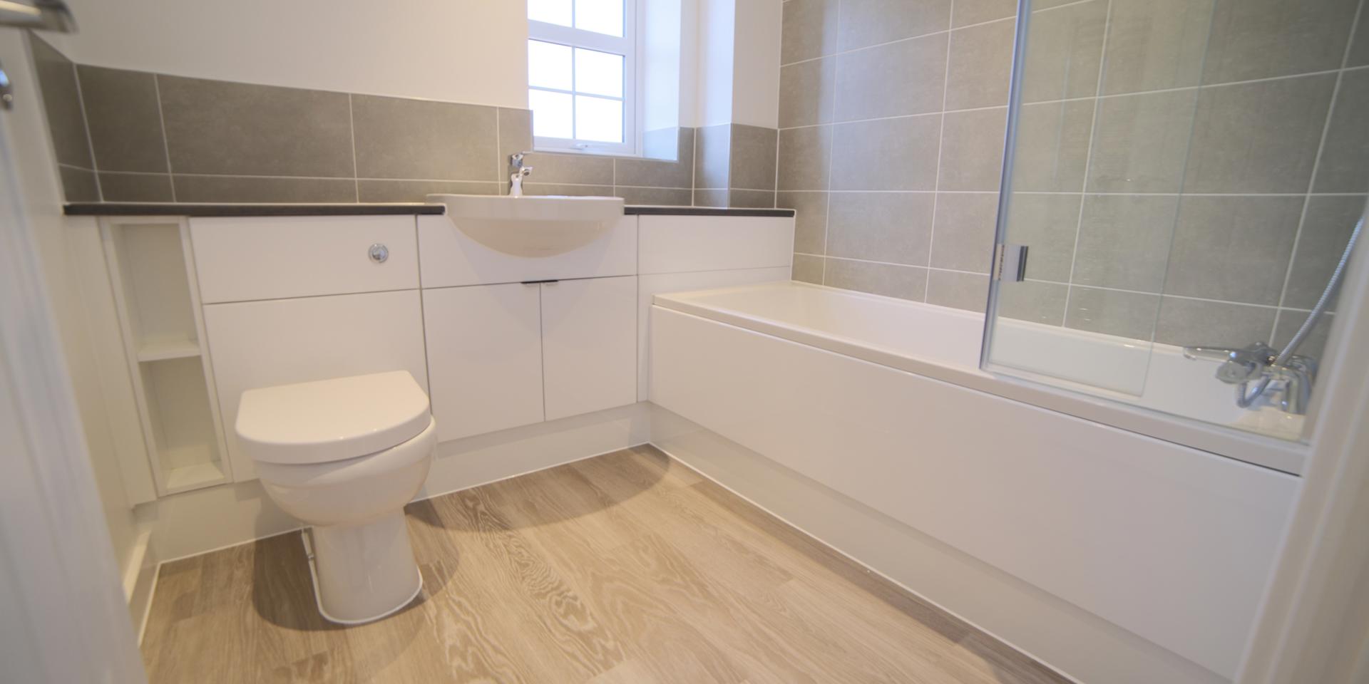 The bathroom has a white suite with built-in vanity unit and glass shower screen to the bath